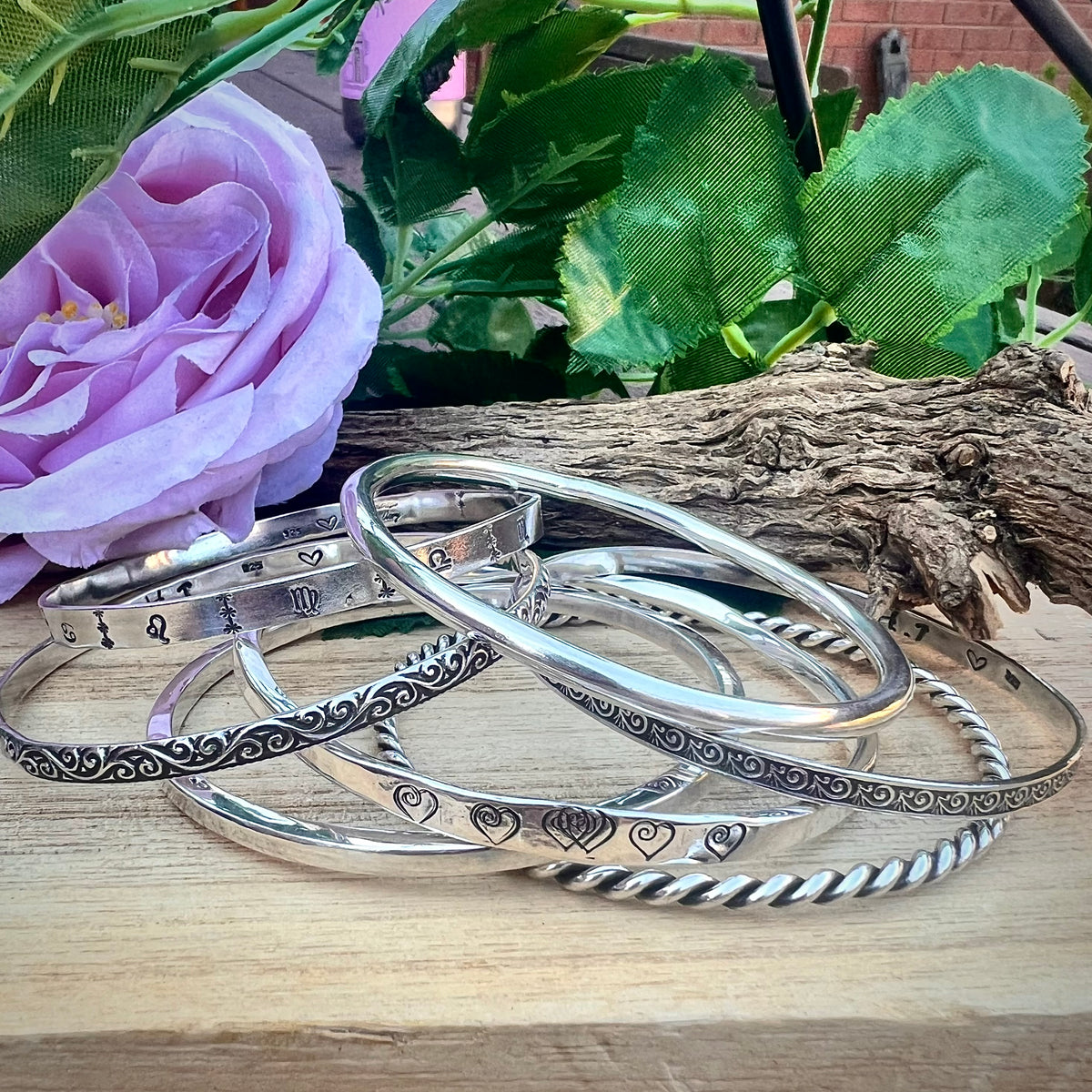 Handmade silver bangles beside a pink rose by Headrush Jewellery